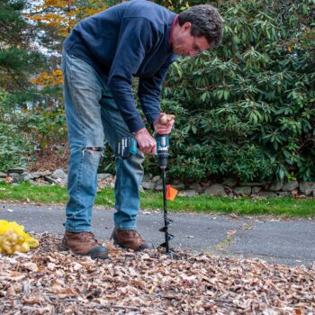A man uses a handheld power drill with a special auger to plant flower bulbs.
